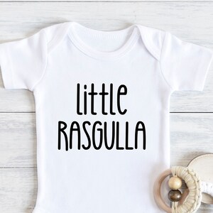 May include: White baby onesie with black text that reads "little rasgulla".
