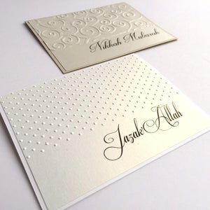 May include: Two white cards with embossed designs. The top card has a swirling pattern and the text "Nikkah Mubarak". The bottom card has a polka dot pattern and the text "Jazak Allah".
