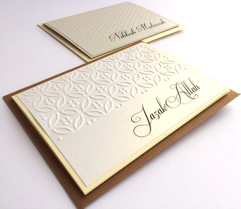 May include: Two white greeting cards with brown envelopes. The top card has a white background with small white dots and the text "Nikkah Mubarak". The bottom card has a white background with a white embossed pattern and the text "Jazak Allah".