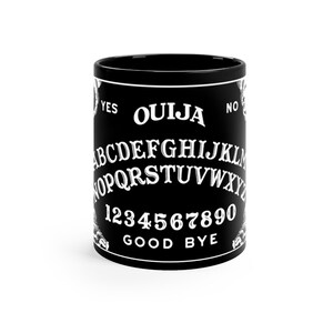 Może przedstawiać: Czarny kubek ceramiczny z białym wzorem planszy Ouija. Wzór zawiera litery alfabetu, cyfry od 1 do 9 i 0 oraz słowa "YES", "NO", "GOOD" i "BYE".
