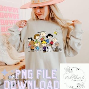 Könnte beinhalten: Hellgraues Sweatshirt mit einem farbenfrohen Aufdruck der Peanuts-Charaktere. Das Bild enthält den Text "PNG FILE DOWNLOAD" in hellem Lila. Ein Wildflower Designs-Logo befindet sich unten rechts.