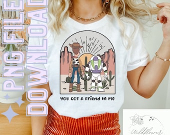 May include: White t-shirt with a cartoon image of Woody and Buzz Lightyear from Toy Story. The image is set against a sunset background with cacti and the text "You got a friend in me".
