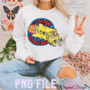 May include: A white sweatshirt featuring a graphic of a yellow school bus flying through the air with the text "The Magic School Bus" in a blue circle.