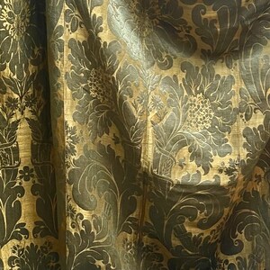 May include: A close-up of a gold fabric with a dark brown floral pattern. The fabric has a subtle sheen and a textured surface.