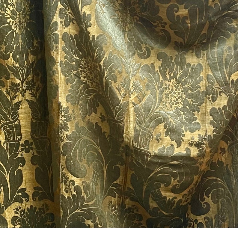 May include: A close-up of a gold fabric with a dark brown floral pattern. The fabric has a subtle sheen and a textured surface.