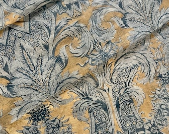 Può includere: Primo piano di un tessuto con un motivo floreale in tonalità di grigio e verde acqua su sfondo giallo dorato. Il design presenta fiori e fogliame stilizzati, creando un'estetica vintage o antica. Il tessuto è probabilmente utilizzato per tappezzeria o tendaggi.
