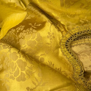 May include: A close-up of a yellow fabric with a floral pattern. The fabric has a gold trim around the edges.