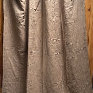 May include: A set of three brown linen curtains hanging on a wooden rod. The curtains are made of a soft, natural fabric and have a subtle texture.