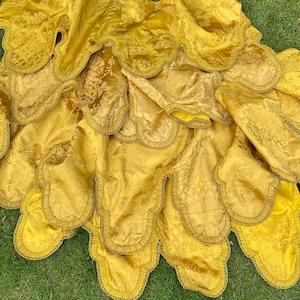 May include: A gold fabric tablecloth with scalloped edges. The tablecloth is layered and has a subtle floral pattern.