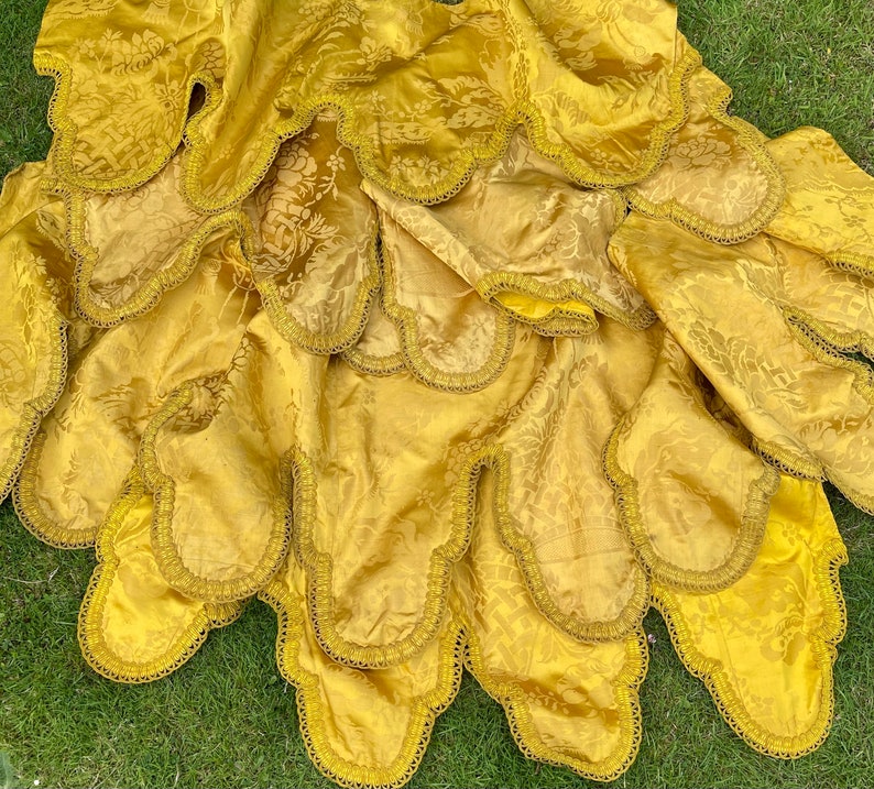 May include: A gold fabric tablecloth with scalloped edges. The tablecloth is layered and has a subtle floral pattern.