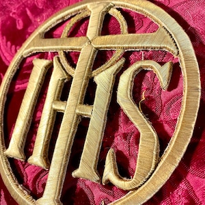 May include: A gold embroidered patch with the letters "IHS" and a cross inside a circle.