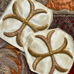 May include: Two cream-colored fabric patches with gold embroidery. Each patch features a six-pointed star design with a gold button in the center.