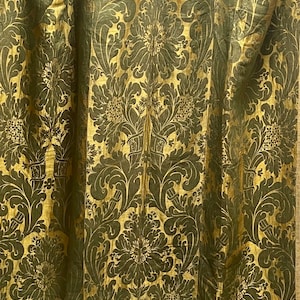 May include: A close-up of a gold and green fabric with a damask pattern. The fabric has a raised texture and a luxurious feel.