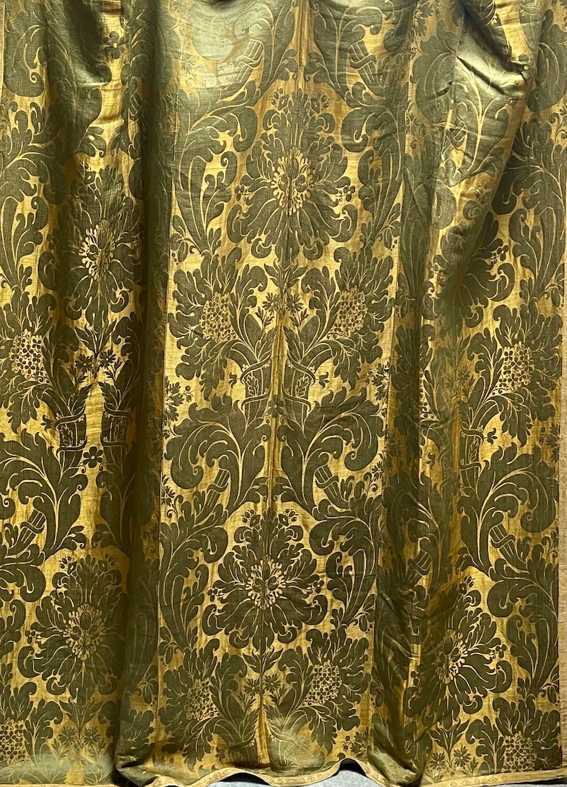 May include: A close-up of a gold and green fabric with a damask pattern. The fabric has a raised texture and a luxurious feel.