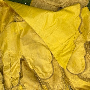 May include: Close-up of a yellow fabric with a decorative trim. The fabric has a subtle pattern and is folded over itself.