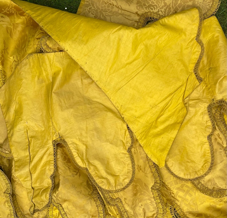 May include: Close-up of a yellow fabric with a decorative trim. The fabric has a subtle pattern and is folded over itself.