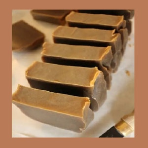 Op de afbeelding: Een stapel van acht bruine stukken zeep op een wit oppervlak. De zeepstukken zijn rechthoekig en hebben een gladde, gepolijste afwerking.