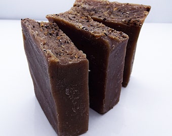May include: Three bars of brown soap with a speckled texture. The soap bars are stacked on top of each other.