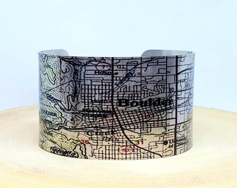 May include: A silver metal cuff bracelet with a black and white map of Boulder, Colorado printed on it. The map shows streets, roads, and landmarks.