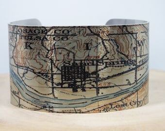 May include: A silver metal cuff bracelet with a vintage map design. The map shows the area around Sand Springs, Oklahoma, with the text "Osage Co", "Tulsa Co", "Sand Springs", and "Lost City".