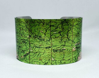 May include: A silver metal cuff bracelet with a green topographic map design. The map features contour lines, elevation markings, and the text "Moscow Mtn 1400 ft".