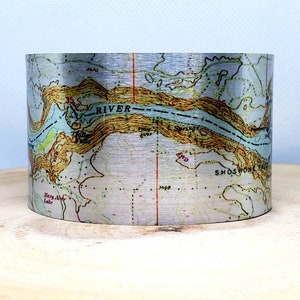 May include: A silver metal cuff bracelet with a vintage map design. The map shows a river and the text "SHOSHONE FALLS".
