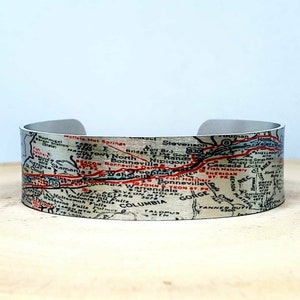 May include: A silver metal cuff bracelet with a vintage map design. The map shows the Columbia River Gorge area of Oregon and Washington. The map features red and black text and lines.