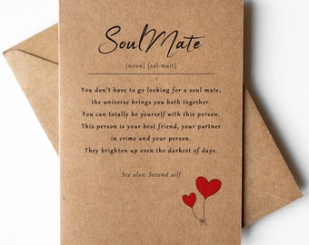 May include: A brown card with the word "Soul Mate" written in cursive. The card defines a soul mate as a person who is your best friend, partner in crime, and your person. The card also says that a soul mate brightens up even the darkest of days. The card has two red hearts with strings attached to them.