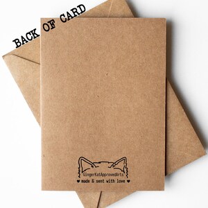 Puede incluir: La parte posterior de una tarjeta marr&oacute;n con una ilustraci&oacute;n en blanco y negro de la cabeza de un gato. El texto "GingerKatApprovedArts" y "made & sent with love" est&aacute;n impresos debajo de la ilustraci&oacute;n.