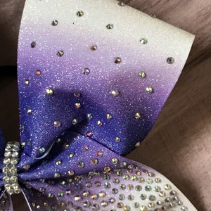 May include: A large purple and white ombre glitter cheer bow with iridescent rhinestones.