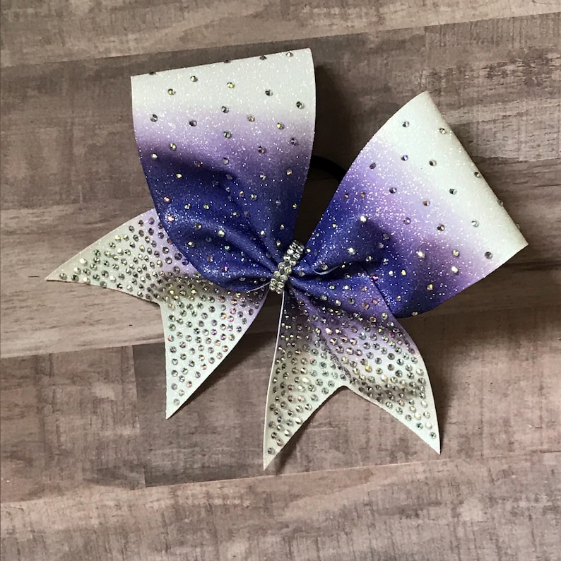 May include: A large purple and white ombre cheer bow with silver glitter and rhinestones.