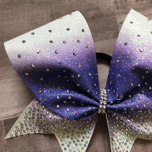 May include: A purple and white ombre cheer bow with silver glitter and rhinestones.