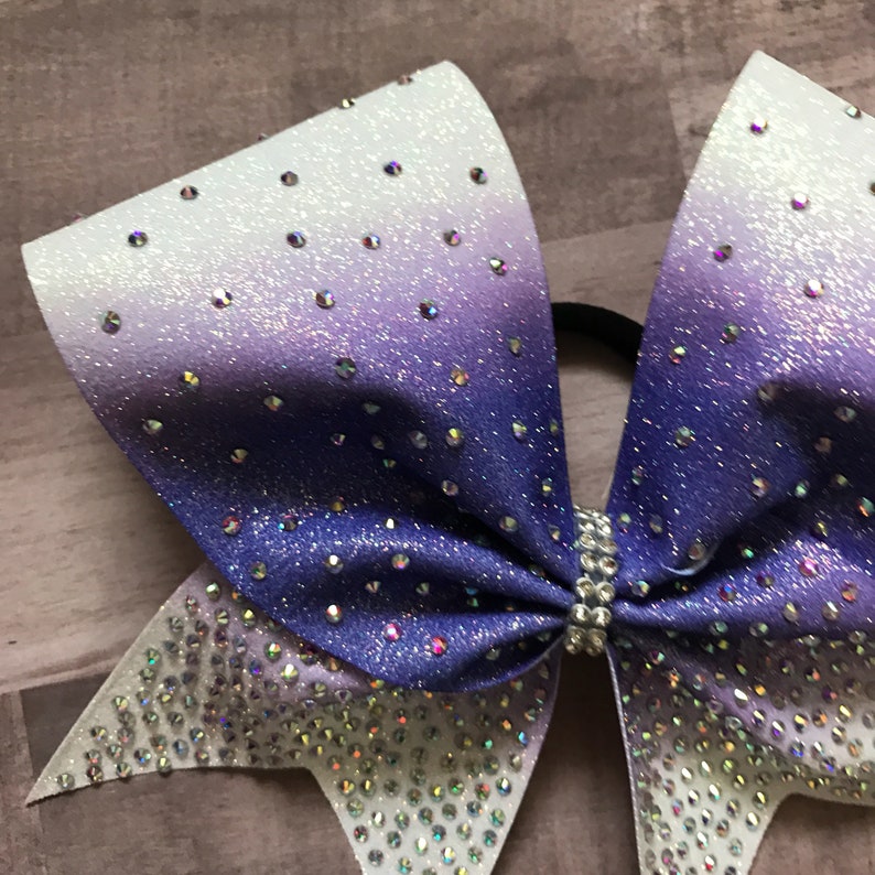 May include: A purple and white ombre cheer bow with silver glitter and rhinestones.