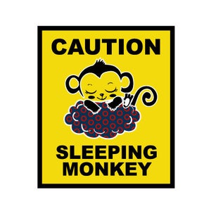 May include: A yellow caution sign with black borders and text. The sign reads "CAUTION SLEEPING MONKEY". A cartoon monkey is sleeping on a blue and red cloud with a donut pattern.