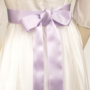 Peut inclure: Une robe blanche avec un ruban de satin lavande noué en un nœud à la taille.