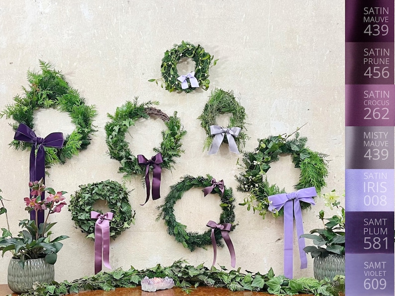 Puede incluir: Ocho coronas hechas de ramas de hoja perenne con cintas de terciopelo y sat&eacute;n de diferentes colores. Las coronas est&aacute;n colgadas en una pared con una carta de colores que muestra diferentes tonos de morado.