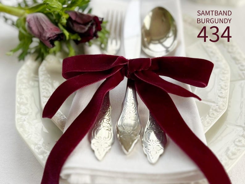 May include: A deep burgundy velvet ribbon tied in a bow around a set of silver-toned metal cutlery, including a fork, knife, and spoon, resting on a white napkin. The text SAMTBAND BURGUNDY 434 is printed in the upper right corner of the image.