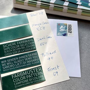 May include: A white card featuring five dark green satin ribbon swatches labeled with handwritten names and numbers, including Petrol 788, Mango Green 858, Dark Green 864, Billiard 911, and Forest 69, alongside a German postage stamp with a bird graphic.