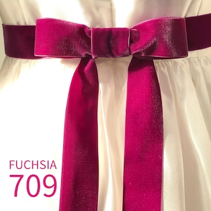 May include: A fuchsia velvet ribbon belt tied in a bow around a white dress. The ribbon features a smooth, soft texture and hangs down in two long tails. The text FUCHSIA 709 is printed in the bottom left corner in a matching fuchsia color.