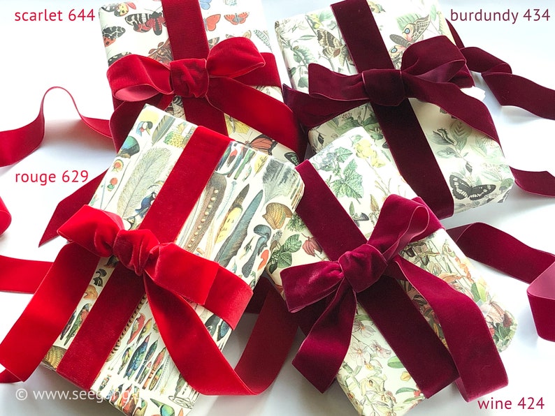 May include: Four rectangular packages wrapped in cream-colored paper featuring botanical and insect illustrations, each tied with a wide velvet ribbon. The ribbons are in shades of scarlet 644, rouge 629, burgundy 434, and wine 424.
