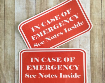 May include: Two red rectangular signs with rounded corners and white text. The top sign says "IN CASE OF EMERGENCY See Notes Inside". The bottom sign says "IN CASE OF EMERGENCY See Notes Inside".