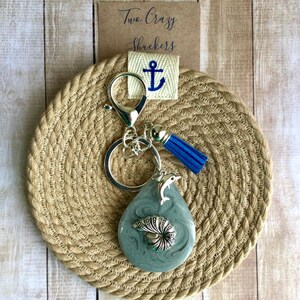 Peut inclure: Un porte-clés en forme d'hippocampe gris et argenté avec un charme en pompon bleu et un charme en ancre argentée. Le porte-clés est sur un dessous de verre en corde tressée avec le texte "Two Crazy Shreckers".