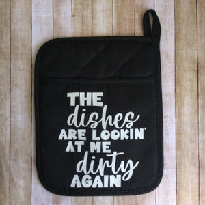Op de afbeelding: Zwarte, gewatteerde ovenwant met witte tekst die "The dishes are lookin' at me dirty again" zegt.