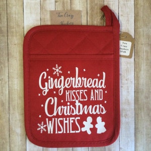 May include: Red quilted pot holder with a white snowflake and gingerbread man design. The text reads "Gingerbread Kisses and Christmas Wishes".