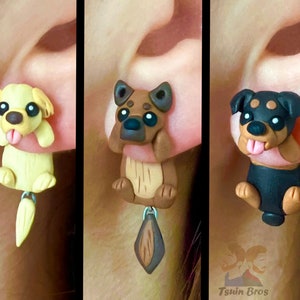 May include: Three pairs of polymer clay earrings featuring different dog breeds. The first pair features a yellow Labrador Retriever, the second pair features a brown and tan German Shepherd, and the third pair features a black and tan Rottweiler.