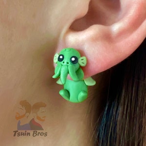 May include: Green and white clay earrings shaped like a cartoon Cthulhu monster with big eyes.