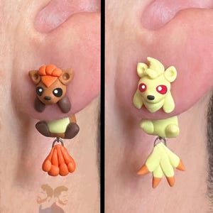Può includere: Orecchini fatti a mano in pasta polimerica raffiguranti personaggi dei cartoni animati. Un orecchino presenta un personaggio marrone e arancione con un ciondolo arancione. L'altro presenta un personaggio giallo con un ciondolo giallo e arancione. Il testo "Tsuin Bros" è visibile.
