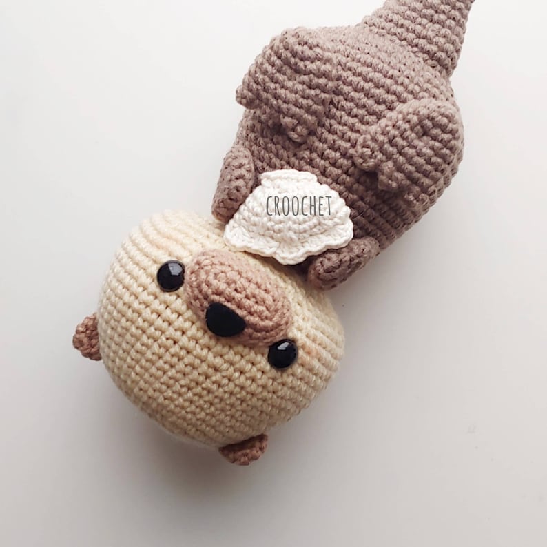 K&ouml;nnte beinhalten: Zwei geh&auml;kelte Stofftiere, eines braun und eines beige. Das braune Tier liegt auf dem beigen Tier. Das beige Tier hat schwarze Augen und eine schwarze Nase. Das braune Tier hat ein wei&szlig;es Etikett mit der Aufschrift "CROOCHET".