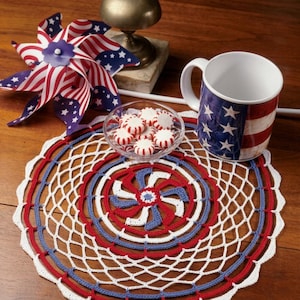 May include: A patriotic-themed still life featuring a red, white, and blue crocheted doily, a mug with an American flag design, a pinwheel, and a small glass bowl of red and white candies. The text "PDF File PATTERN" is visible.