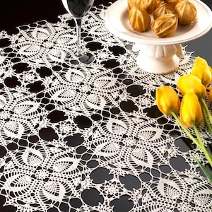 Puede incluir: Un mantel de encaje de ganchillo blanco con un intrincado patrón repetitivo de flores y hojas. El texto PDF File Pattern es visible en la esquina superior izquierda. El encaje se muestra con un vaso de agua, un cuenco blanco con pedestal y tulipanes amarillos.